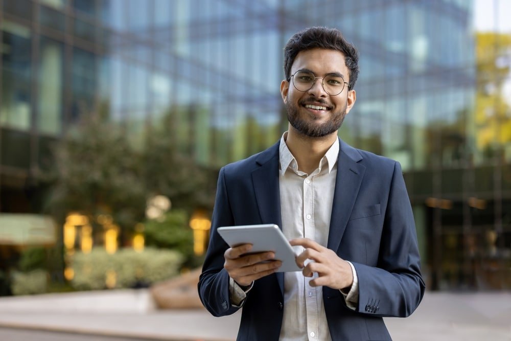 Young,Businessman,In,Suit,Using,Tablet,Outside,Modern,Glass,Office